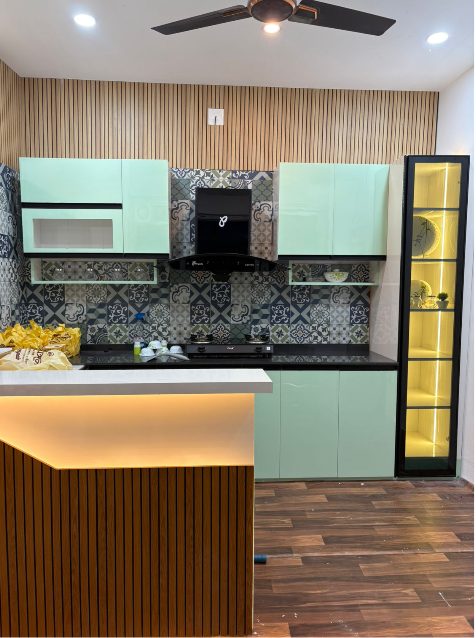Mint-green modular kitchen with patterned tile backsplash, fluted wood panelling and lit display unit